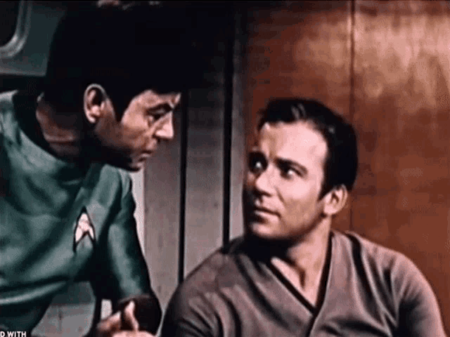 two men are sitting next to each other and one of them is wearing a shirt that says star trek on it .