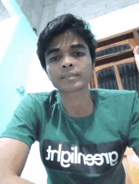 a man wearing a green t-shirt that says trlpilneenp looks at the camera