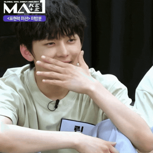 a young man covering his mouth with his hand while wearing a shirt that says make