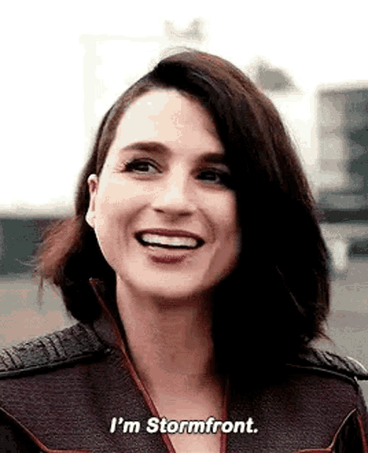 a woman is smiling and saying `` i 'm stormfront '' while standing in front of a building .