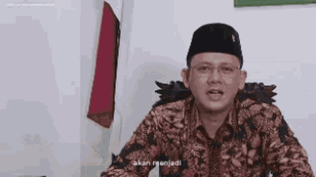 a man wearing a hat and a floral shirt is sitting at a desk .