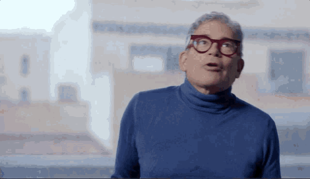 a man wearing glasses and a blue turtleneck is looking up