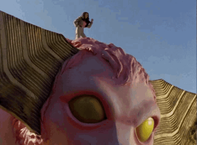a woman is standing on top of a pink sculpture with yellow eyes