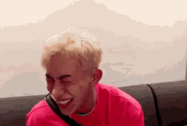 a man in a pink shirt is sitting on a couch laughing .