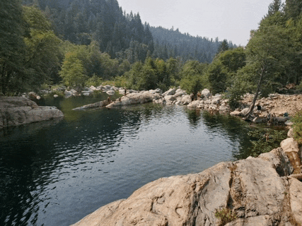 a body of water surrounded by rocks and trees with mountains in the background