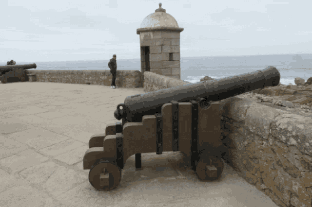 a man stands behind a cannon on a ledge overlooking the ocean