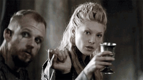 a man and a woman are sitting at a table . the woman is holding a glass of wine and pointing at the man .