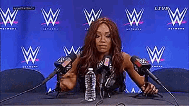 a woman is sitting at a table with microphones and a water bottle