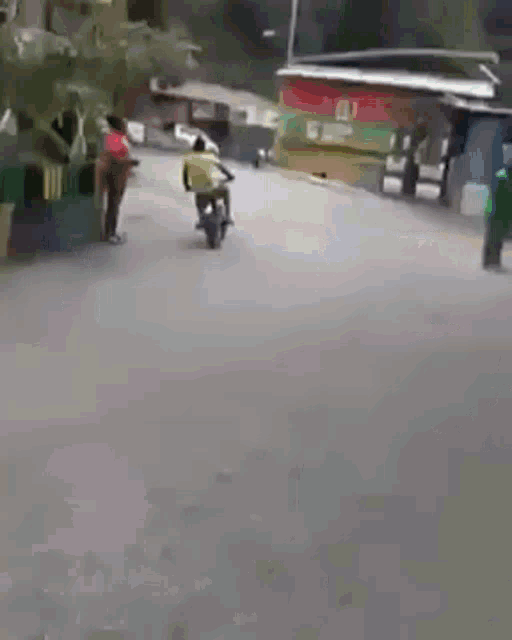 a man is riding a motorcycle down a street while another man stands behind him .