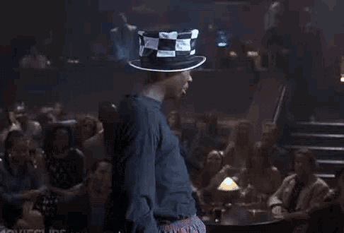 a man in a top hat is dancing in front of a crowd of people in a club .