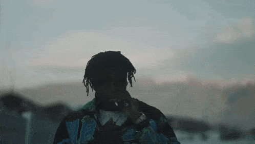a man with dreadlocks is smoking a cigarette while standing in front of a body of water .