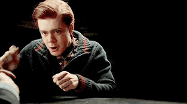 a young man with red hair is sitting at a table with a book in his hand .