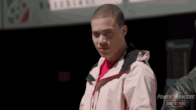 a man in a pink power rangers jacket stands in front of a sign that says dino fury