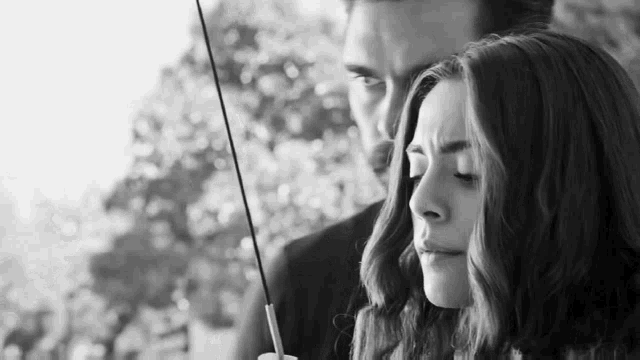a man and a woman are standing next to each other holding an umbrella in a black and white photo .