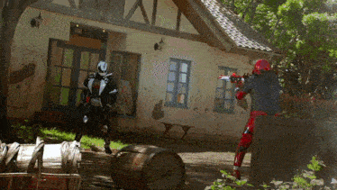 a man in a red and black costume is holding a gun in front of a house