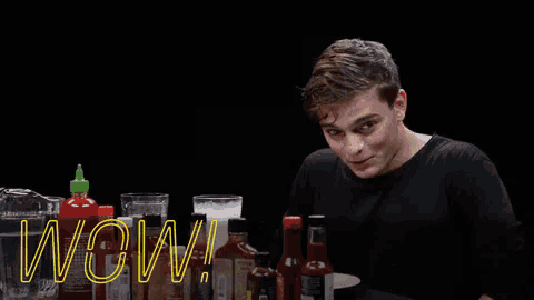 a man sitting at a table with a bottle of hot sauce and a bottle of beer