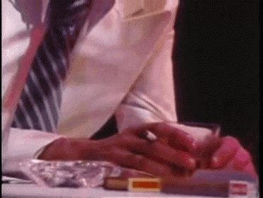 a man in a suit and tie is smoking a cigarette next to an ashtray