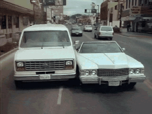 a ford van and a cadillac are driving down the street