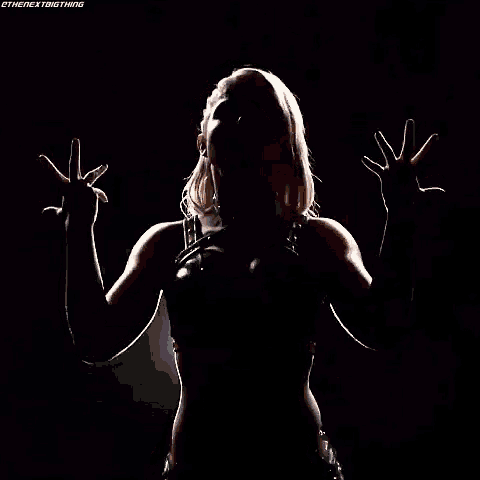 a woman is standing in the dark with her hands up in the air .