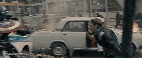 captain america is getting out of a car while holding his shield .
