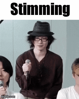 a man wearing a hat and glasses is holding a microphone in front of a sign that says " stunning "