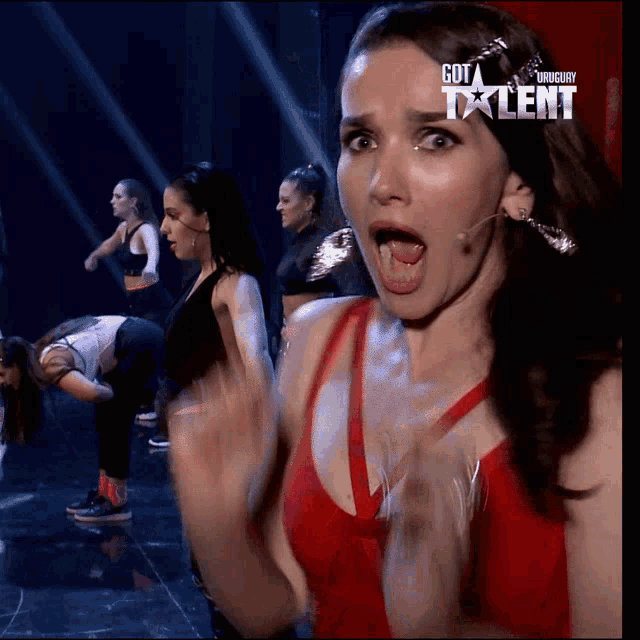 a woman with a surprised look on her face is in front of a group of dancers on a screen that says got talent