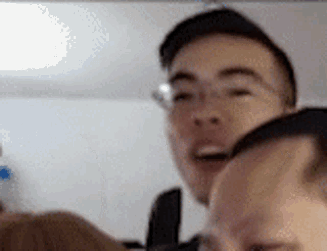a man wearing glasses is looking at the camera while another man looks on .