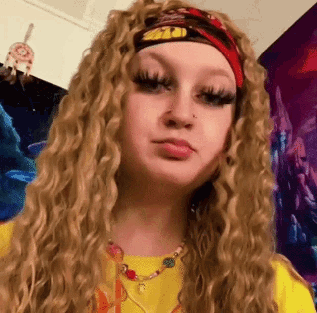 a woman with curly blonde hair is wearing a headband and a necklace .