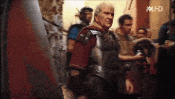 a man in armor is standing in front of a group of men and the number 16 hd is on the bottom of the screen