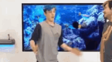a man with blue hair is standing in front of a large screen .