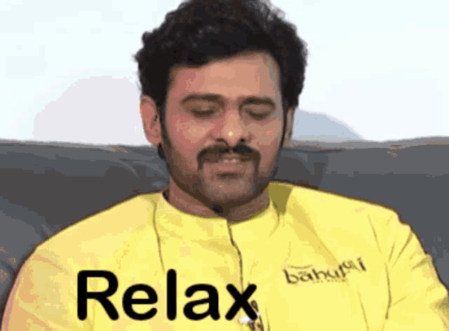 a man with a mustache is sitting on a couch with the word relax written on his shirt