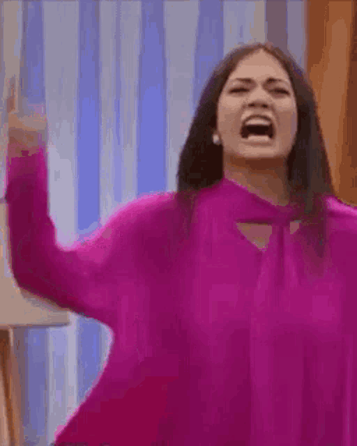 a woman in a purple sweater is screaming with her mouth open and her hand in the air .