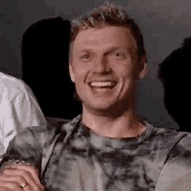a man in a tie dye shirt is smiling while sitting in a dark room .
