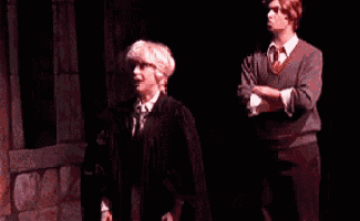 a man in a graduation cap and gown is standing next to a man in a sweater and tie on a stage .