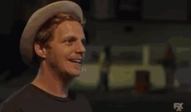 a man wearing a hat and smiling is standing in front of a fire .