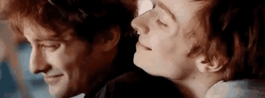 two men are laying next to each other on a bed and smiling .