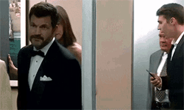a man in a tuxedo is standing in a hallway with a woman behind him