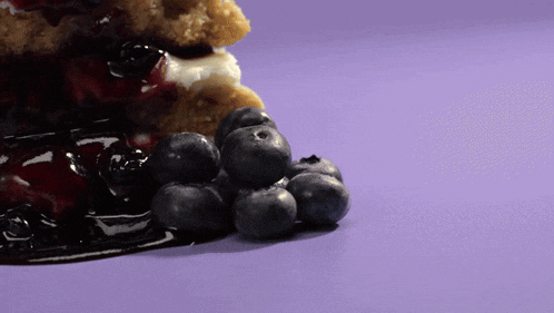 a purple surface with blueberries and a piece of cake
