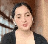 a woman wearing ear buds and a black shirt is looking at the camera .