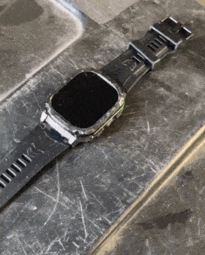 a watch with a black band and a black face is laying on a dirty surface