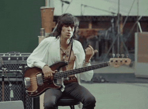 a man is playing a bass guitar while sitting on a stool