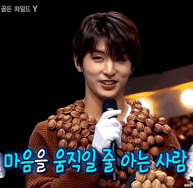 a man wearing a sweater with nuts on it holds a microphone