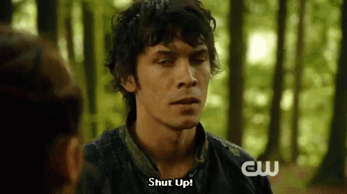 a man in a black shirt is talking to a woman in the woods and says `` shut up '' .