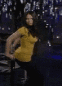 a woman in a yellow shirt is standing in a dark room with her hands on her hips