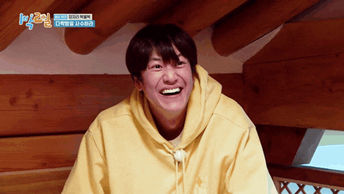 a man wearing a yellow hoodie is smiling in front of a sign that says ' k2 '