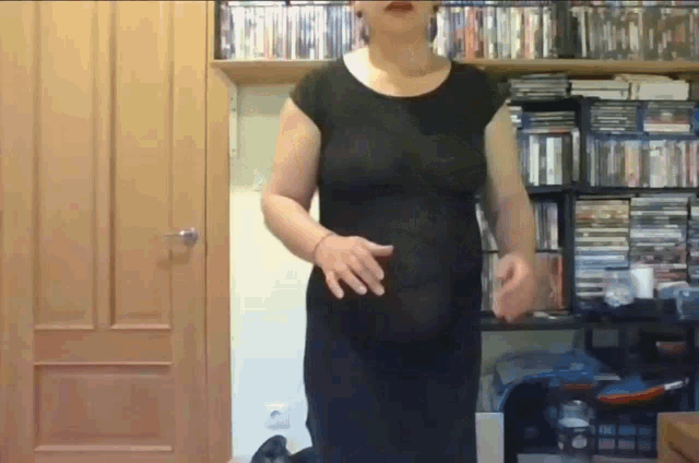 a woman in a black dress is standing in front of a shelf of dvds