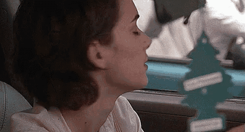 a woman is sitting in a car smelling a christmas tree .