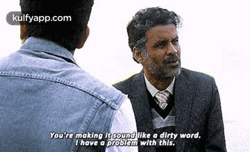 a man in a suit and tie is talking to another man in a denim shirt .