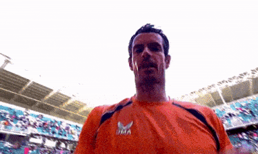 a man wearing an orange shirt with the letter m on the front