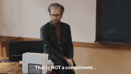 a man in a suit sits at a desk with the words that is not a compliment